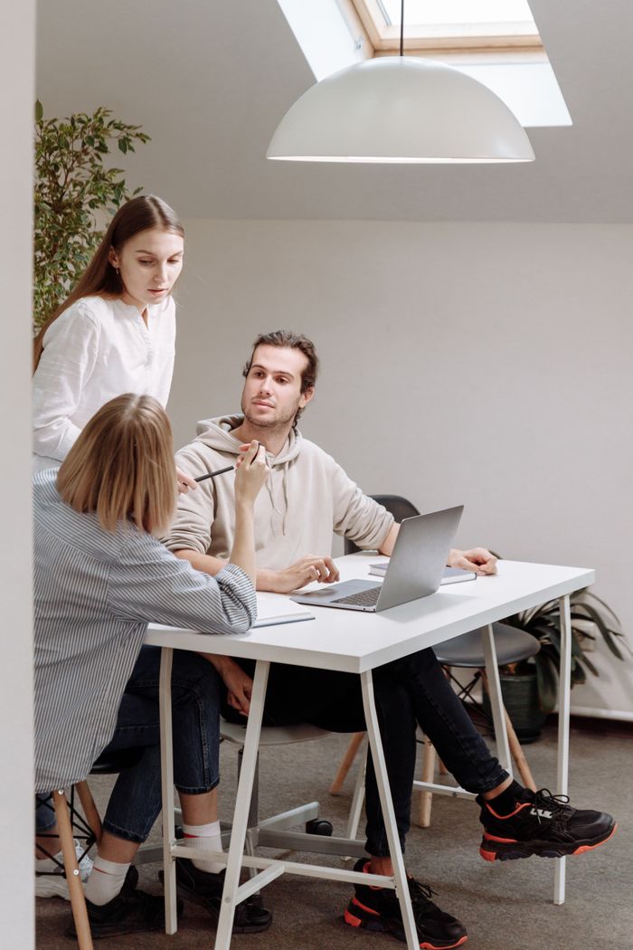 Three colleagues engage in a collaborative meeting around a table in a bright office space.