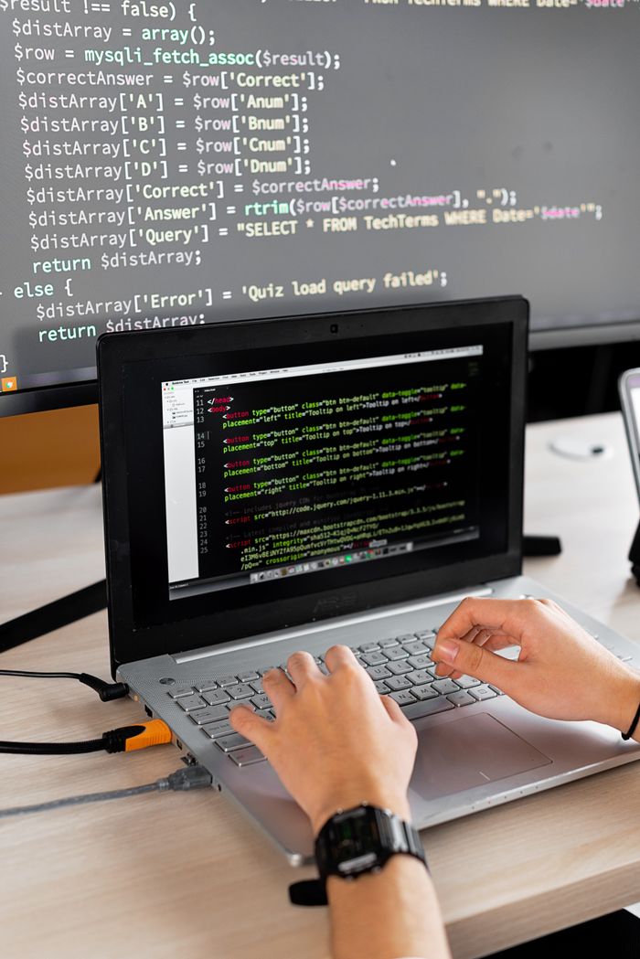 services-06 Person coding at a desk with laptop and external monitor showing programming code.